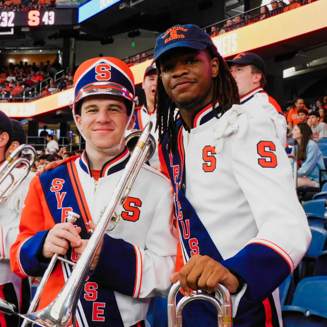 Two individuals hold instruments and smile.