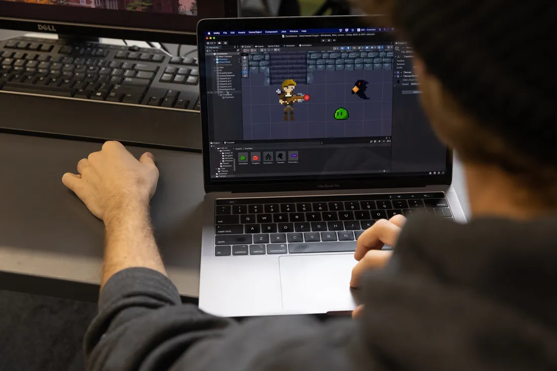 Two hands work on a laptop that has a computer game on the screen.