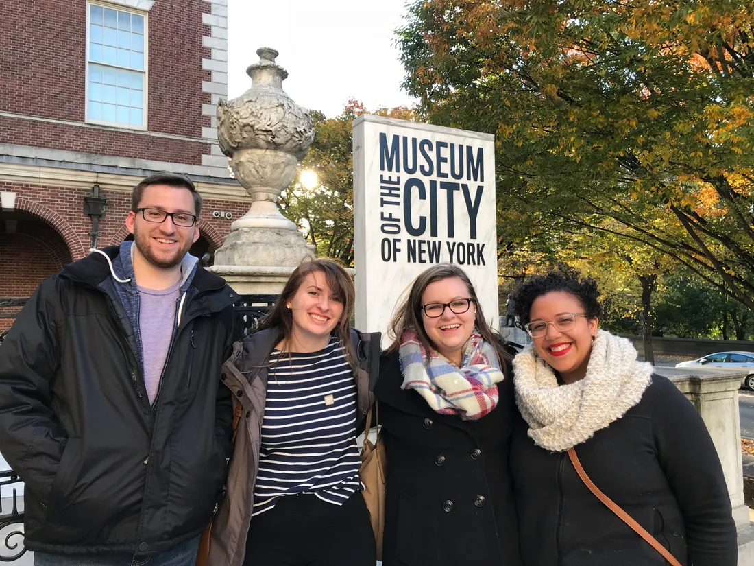 Four people pose and smile in front of a sign that says Museum of the City of New York.