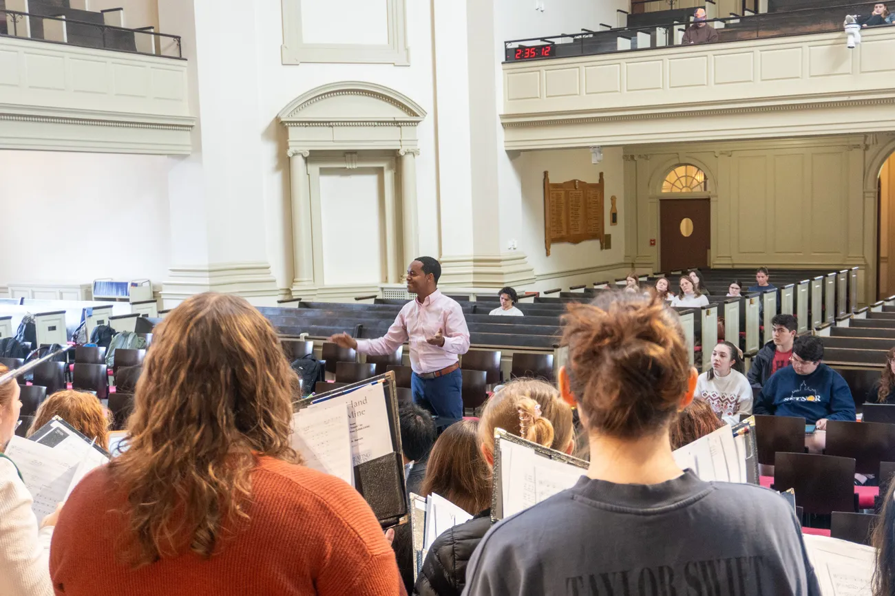 A person conducts a choir in rehearsal in a chapel sanctuary.