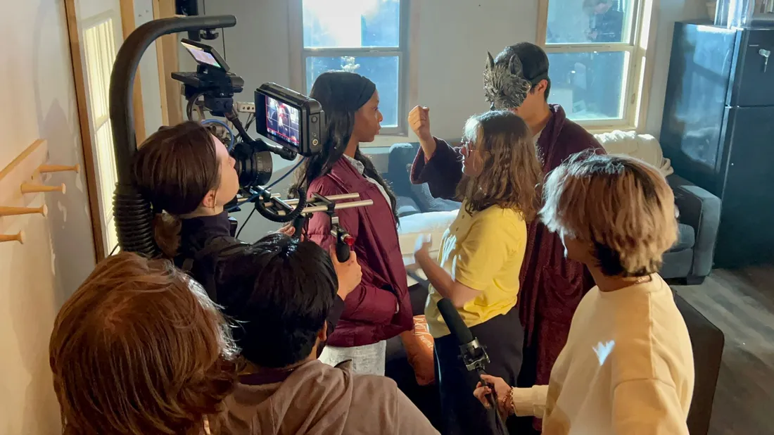 A group of students on the set of a film shoot. Some of the students are actors, while others hold filmmaking equipment.