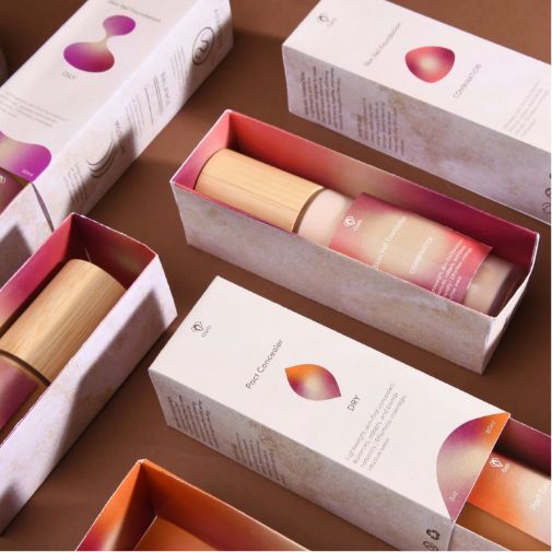 A collection of cosmetic skincare packaging boxes and bottles arranged on a warm brown surface, featuring soft pink, orange, and cream gradients with minimalist branding and wooden caps. Several boxes are open to reveal the products inside, creating a clean, modern beauty packaging presentation.