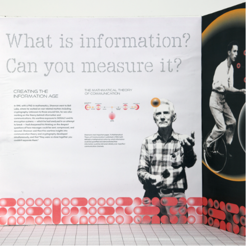 A modern exhibition wall display explores the concept of information theory with large text reading “What is information? Can you measure it?” The exhibit features historical imagery, including a man juggling and another performing on a unicycle, alongside diagrams, explanatory text, and bold abstract red graphic elements in a clean museum-style setting.