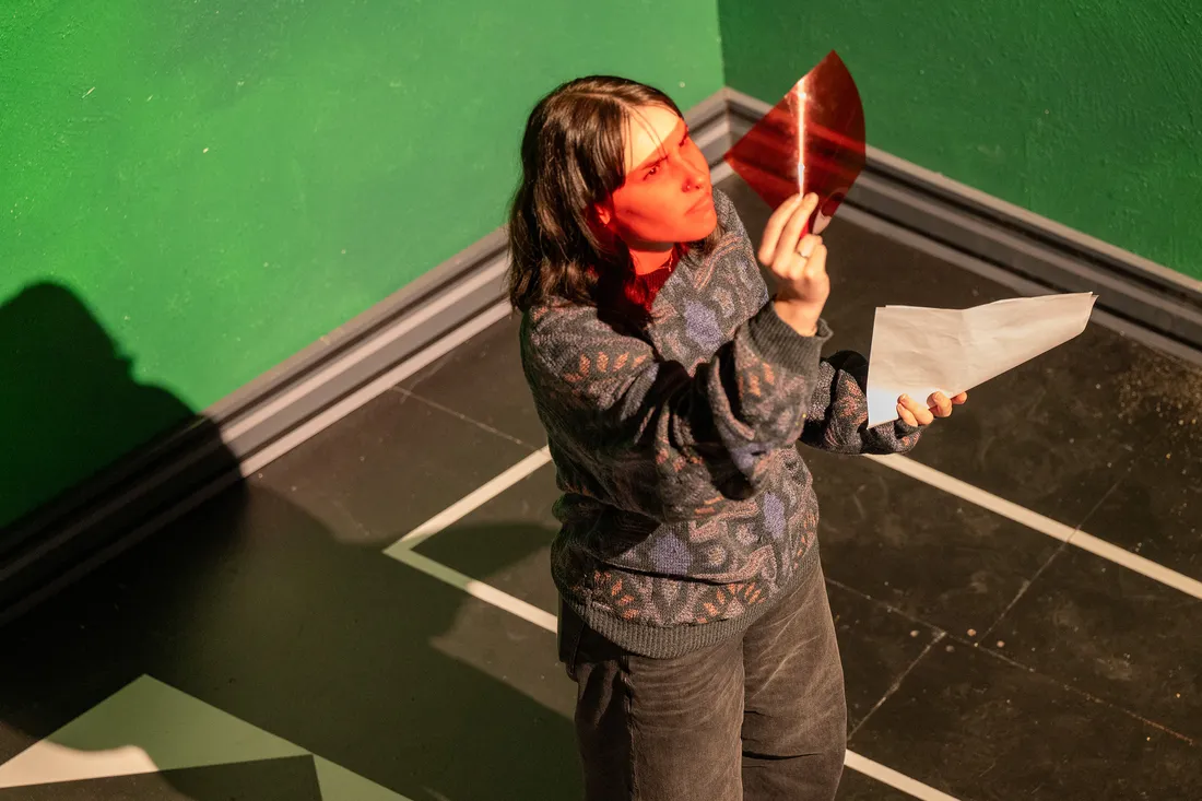 A student holds a red film paper up to the light on a stage.
