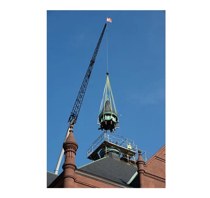 A crane lifts one of the cupolas off Crouse College in the sky.