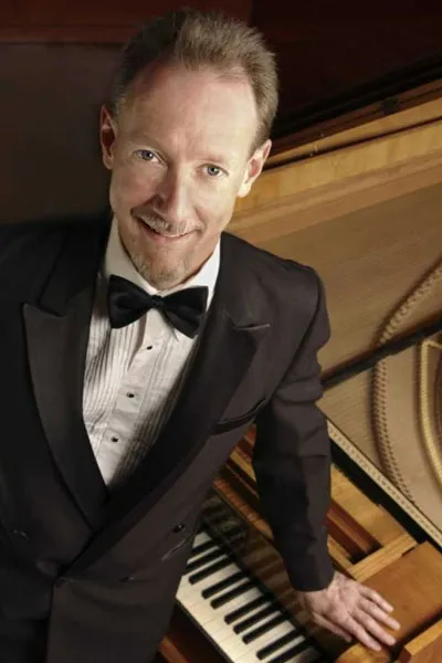 Andrew Willis stands beside a piano.