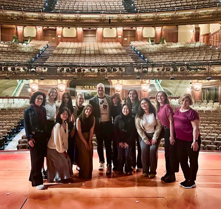 A group of people pose and smile on stage in a theater.