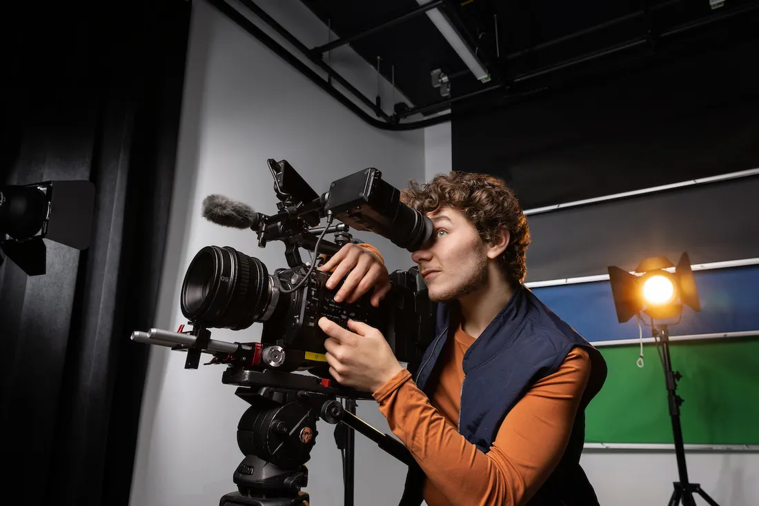 A student looks into the lens of a camera in a film studio.