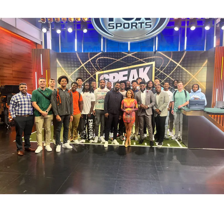 A group of people pose on a television sound stage.