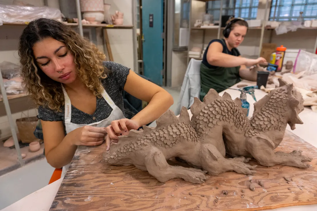 A student sculpts a dragon out of clay.