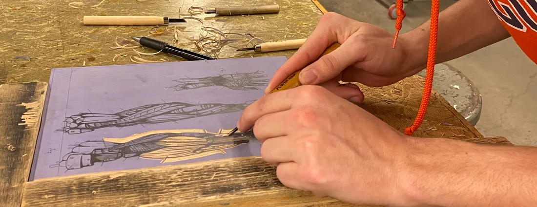 Two hands work on an etching on a table.