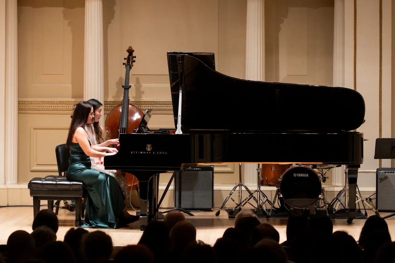 Two people in formal dress sit at a piano and play.