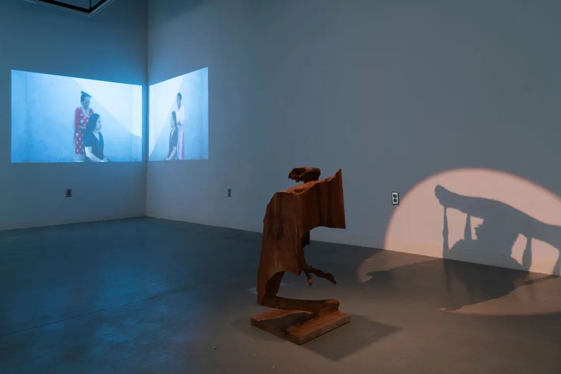 A sculpture and a projection of photography on a wall in a gallery.