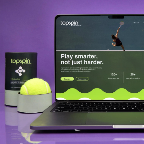 A modern sports technology product display featuring a laptop showcasing the “Topspin” tennis training website with the headline “Play smarter, not just harder.” Beside the laptop are a branded tennis ball container and a bright yellow tennis ball, all set against a sleek purple background with clean, contemporary styling.