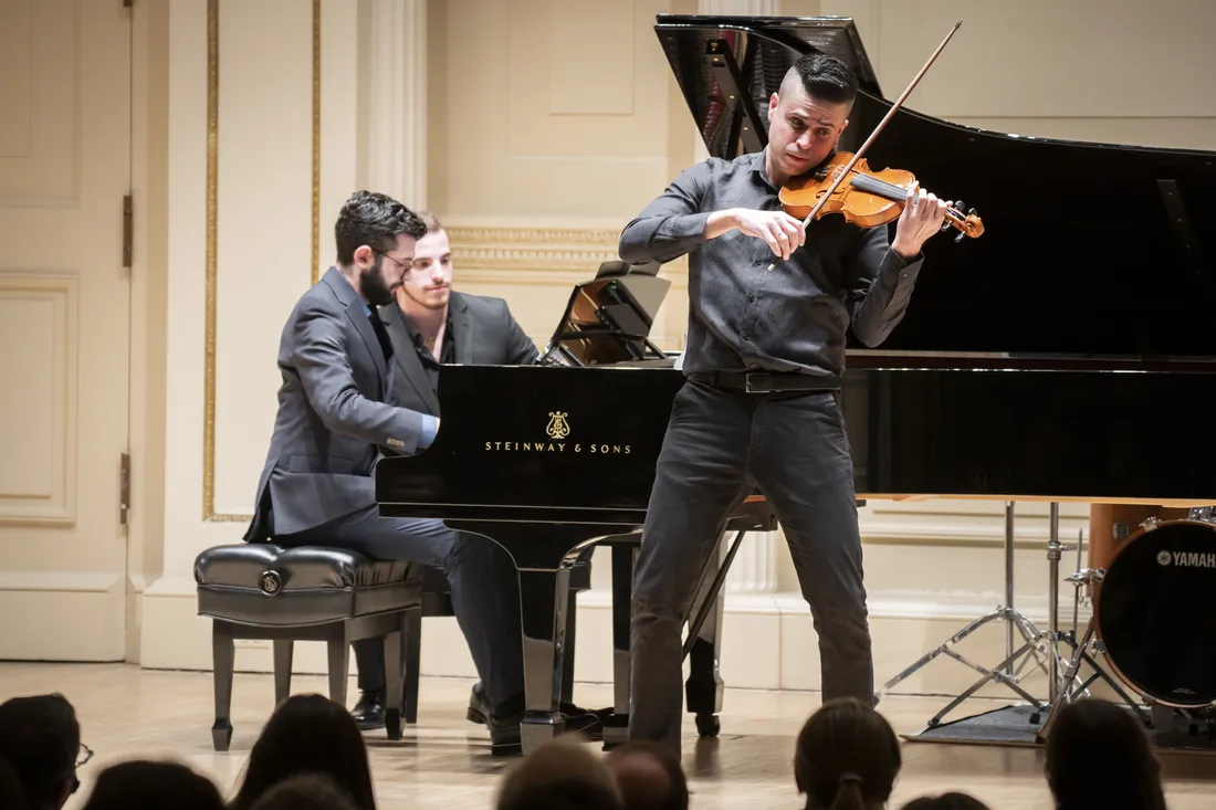 A violinist and a pianist perform on stage.