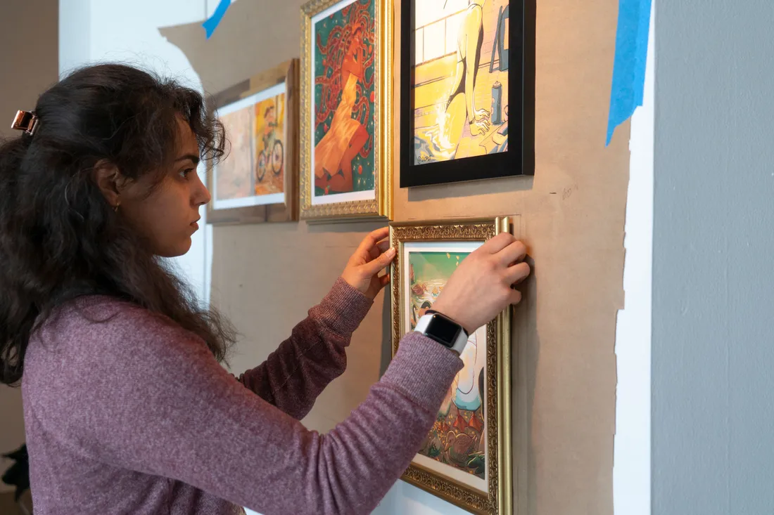A student hangs a painting on a wall.