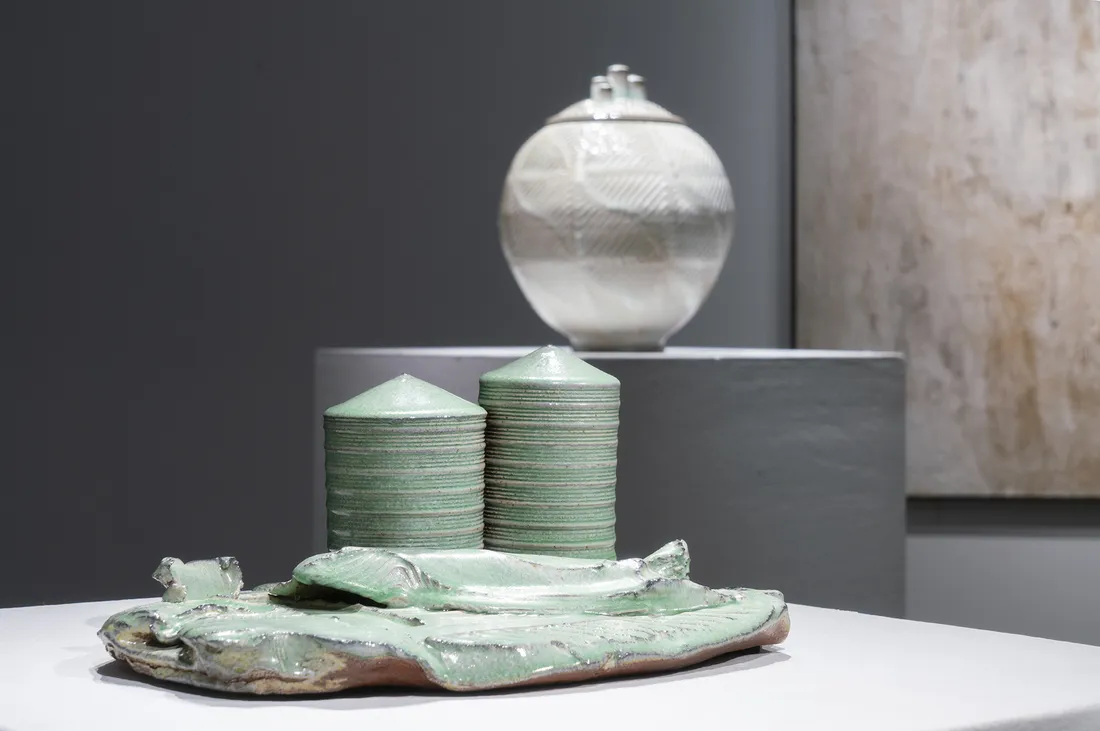 Two pieces of ceramic work by David Hiltner. One is a round vessel on a pedestal. The other is a green sculptural piece with two cylinders.