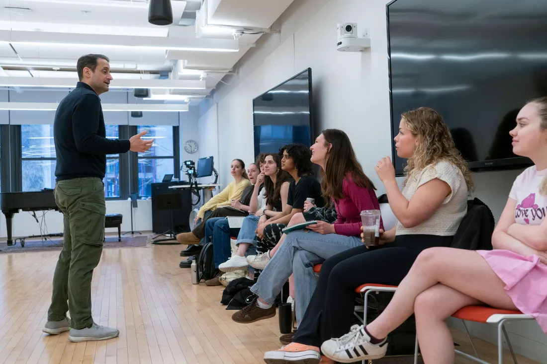 A faculty member stands in front of a line of students who are seated.