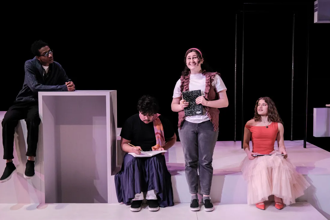 Four actors dressed in contemporary clothing act out a scene on a minimal, white stage.
