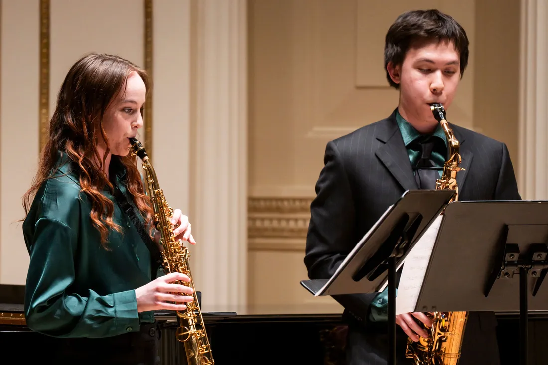 Two people play saxophones.