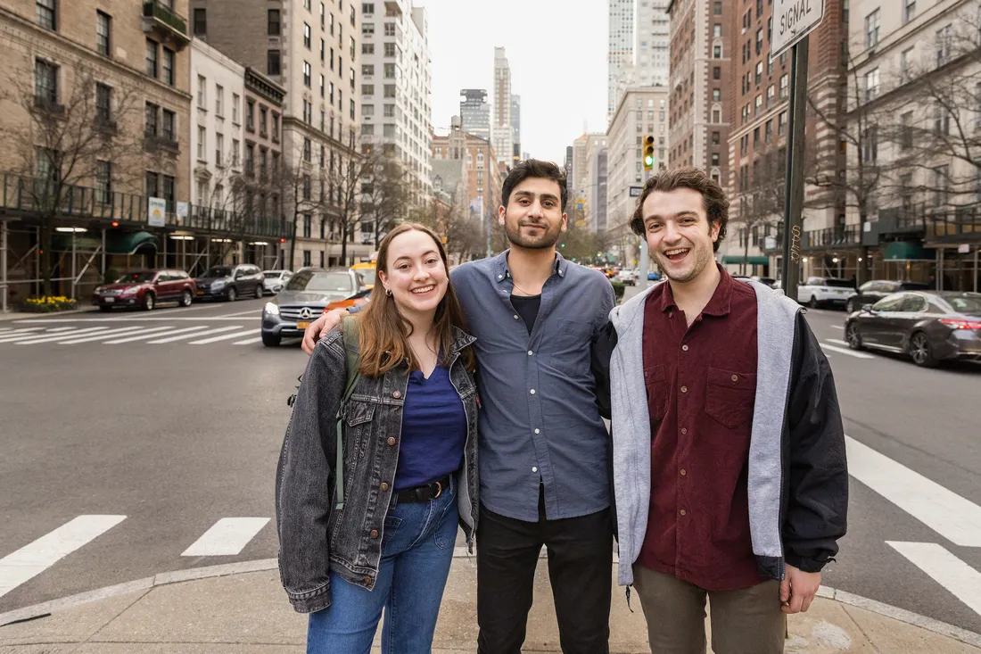 Three students pose and smile on a street in New York City.