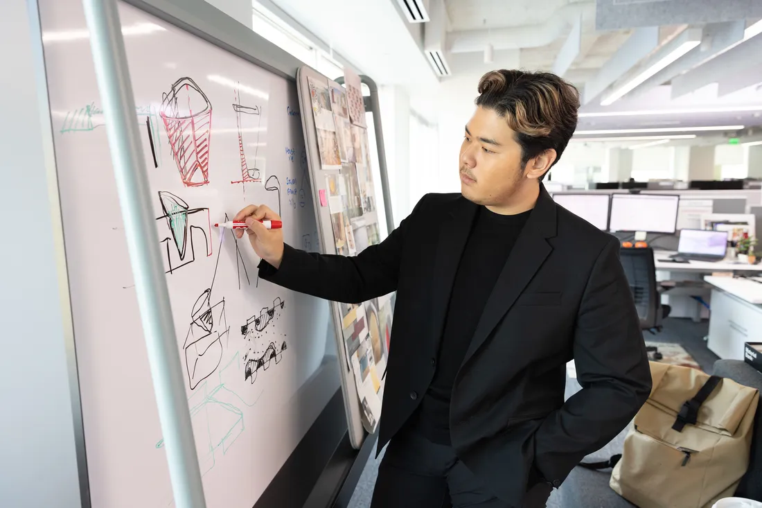 A student stands at a white board drawing a design.