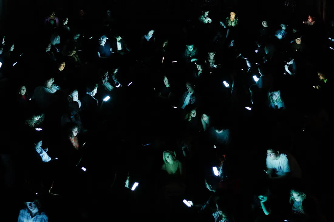 People sit in a dark room only illuminated by the glow of their mobile phones.