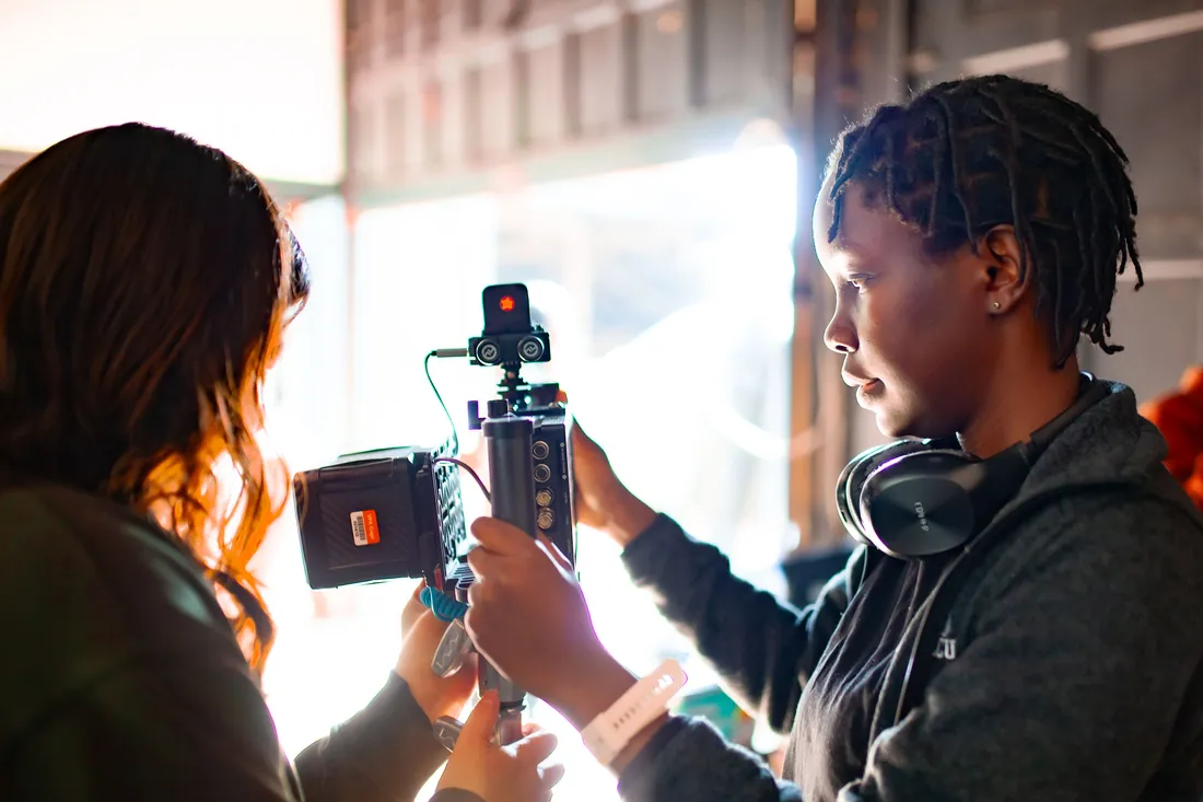 Two students hold a piece of equipment on the set of a film shoot.